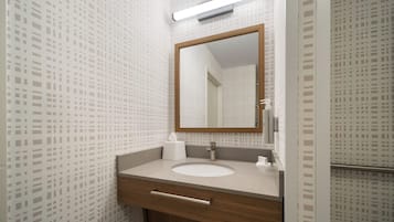 Un baño con tocador de madera, lavamanos blanco, espejo y papel tapiz estampado.