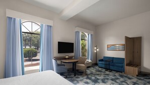 A hotel room with a bed, a desk with a chair, a sofa, a TV, and a window with curtains.