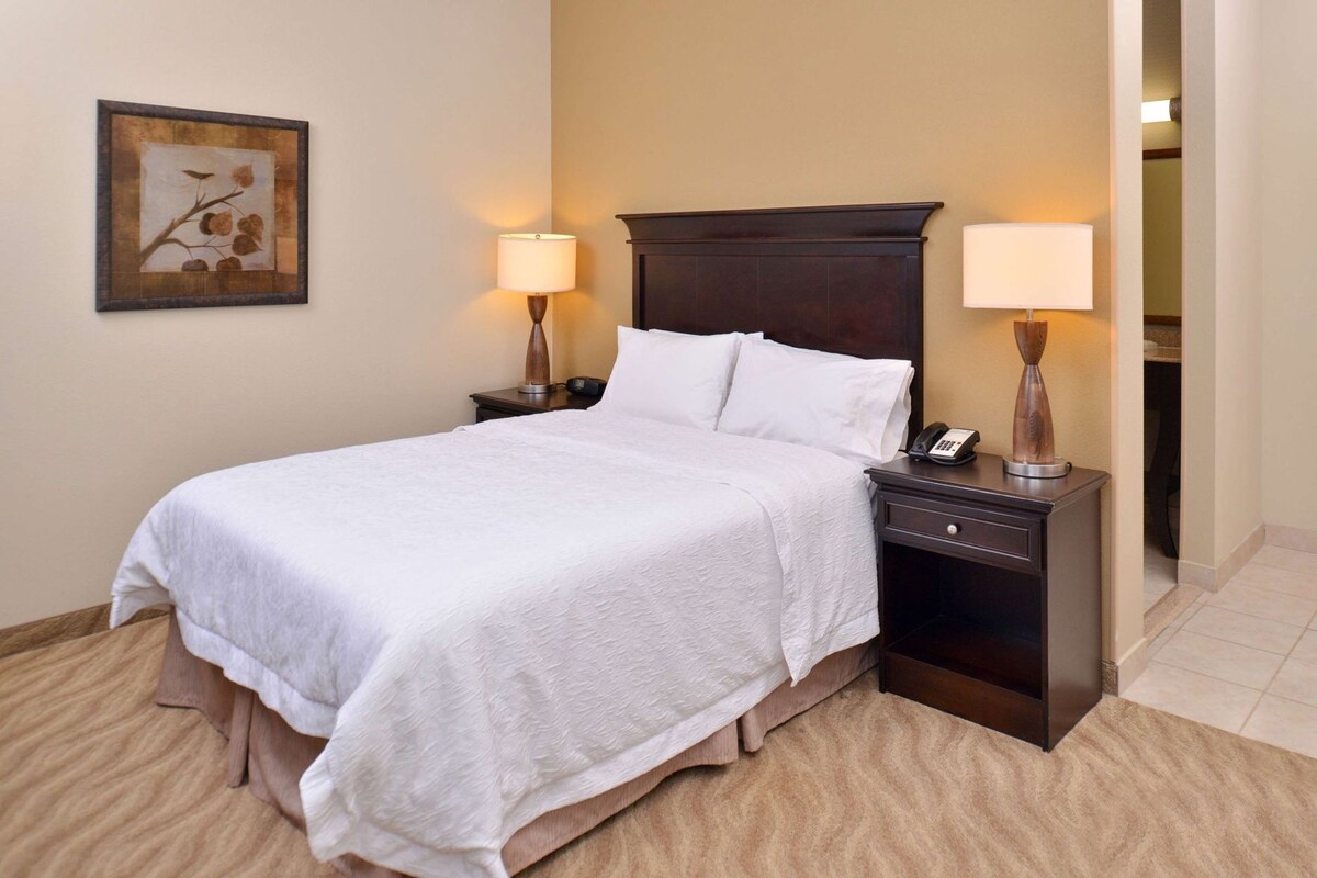 A hotel room with a bed, two bedside tables with lamps, a telephone, and a framed picture on the wall.