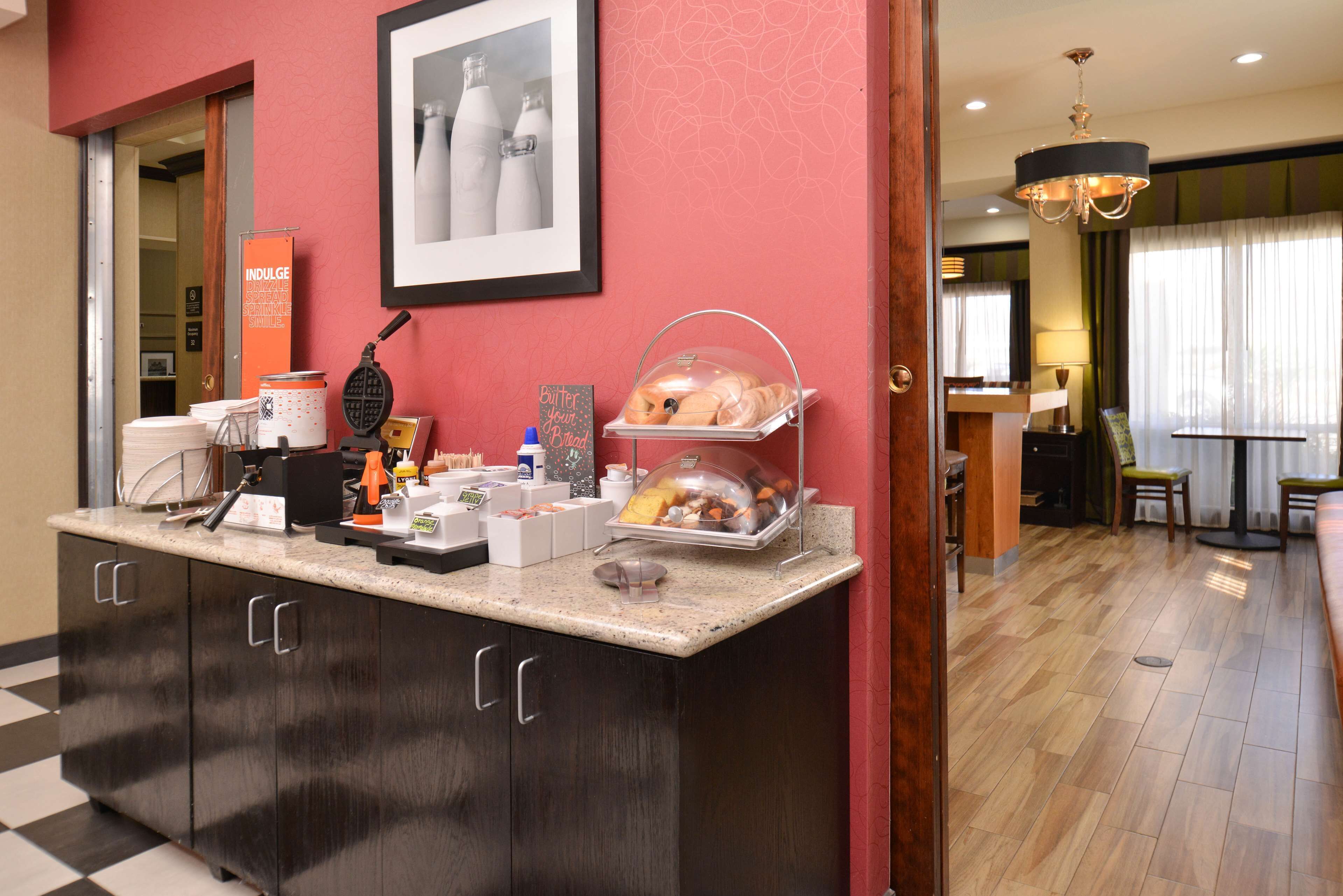 Un área de desayuno de hotel con mostrador, máquina de café y diversos alimentos.