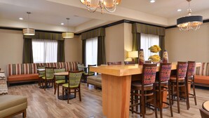 A hotel lobby with a wooden bar, green and patterned chairs, a sofa, and a dining area with a wooden table and chairs. - Hampton Inn Van Horn (Van Horn)