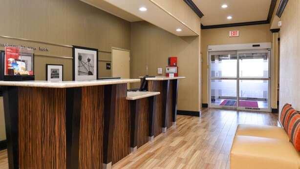 A reception area with a wooden reception desk, framed pictures on the wall, and a sofa in the background. - Hampton Inn Van Horn (Van Horn)