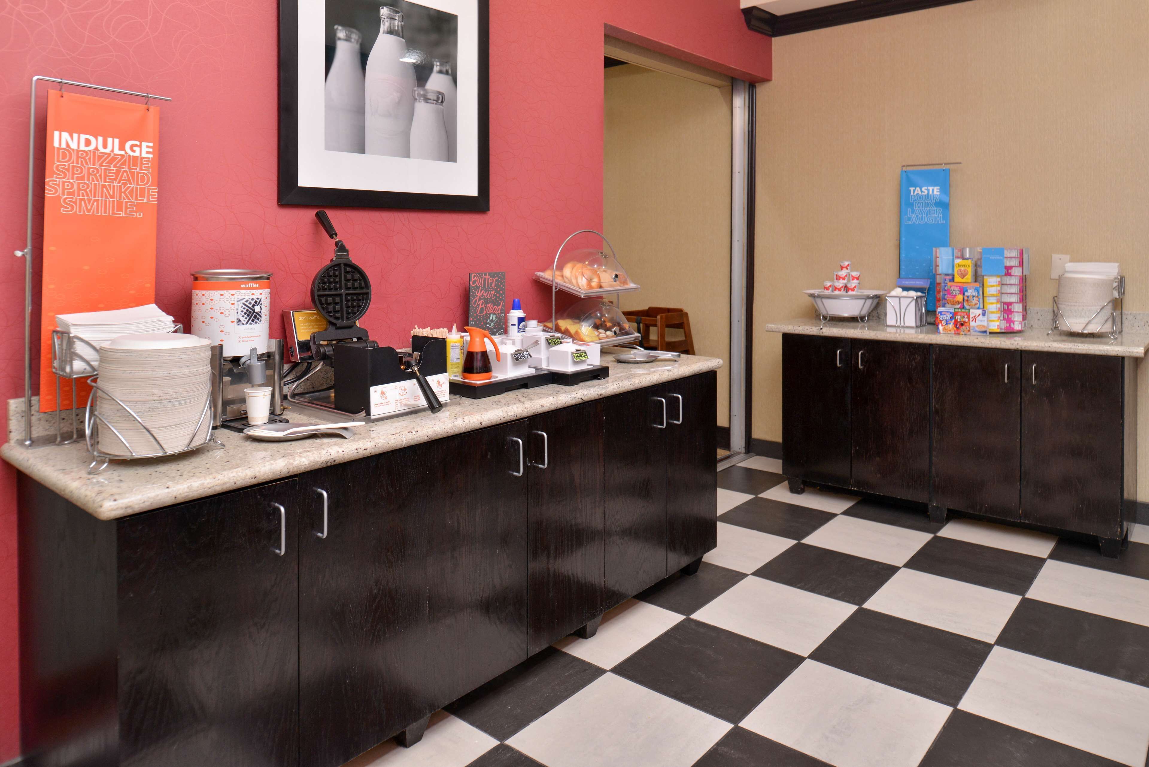 A breakfast bar with a waffle maker, coffee station, and various food items.