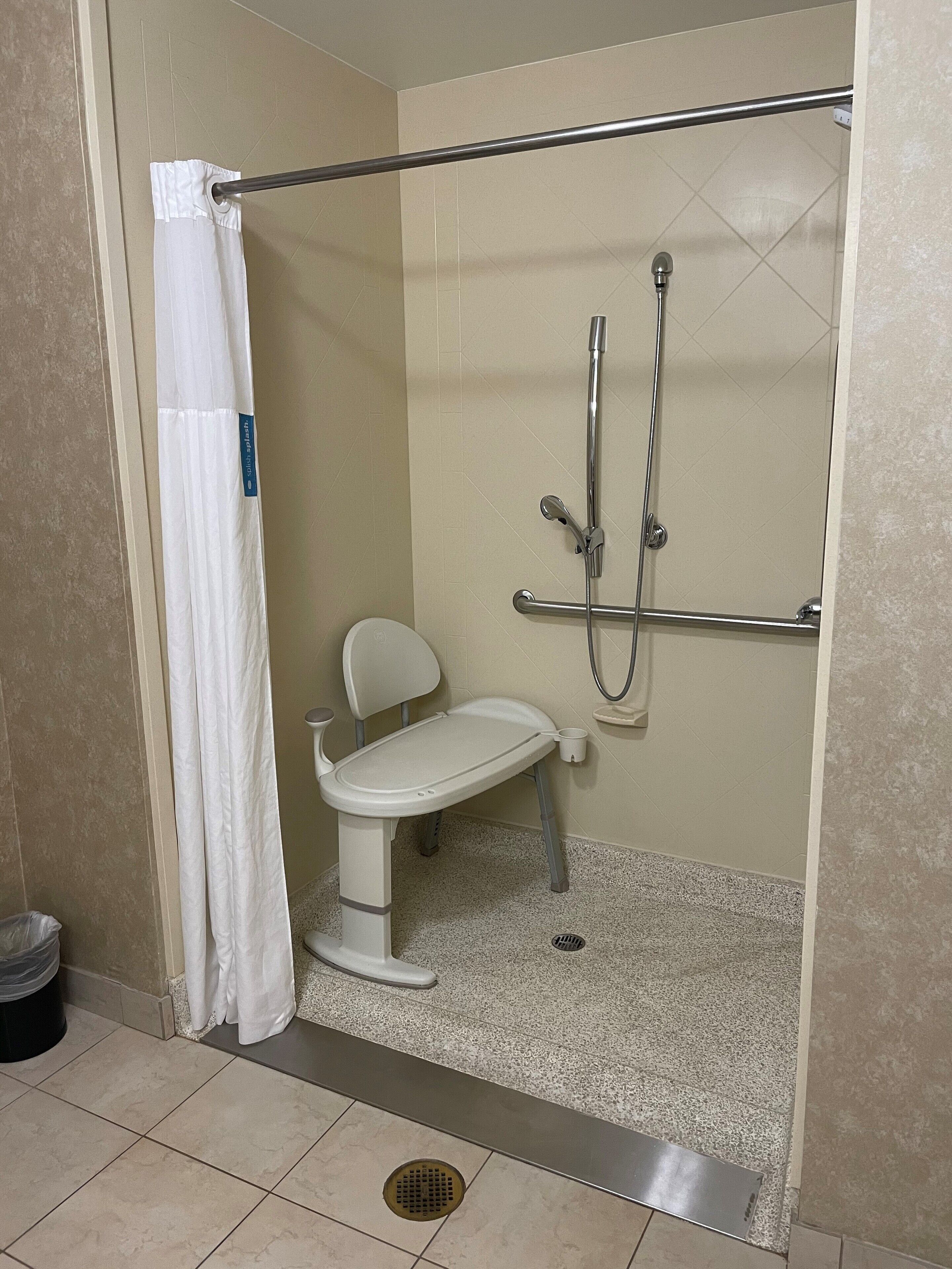 A small, enclosed shower area with a white toilet, a showerhead, and a grab bar.