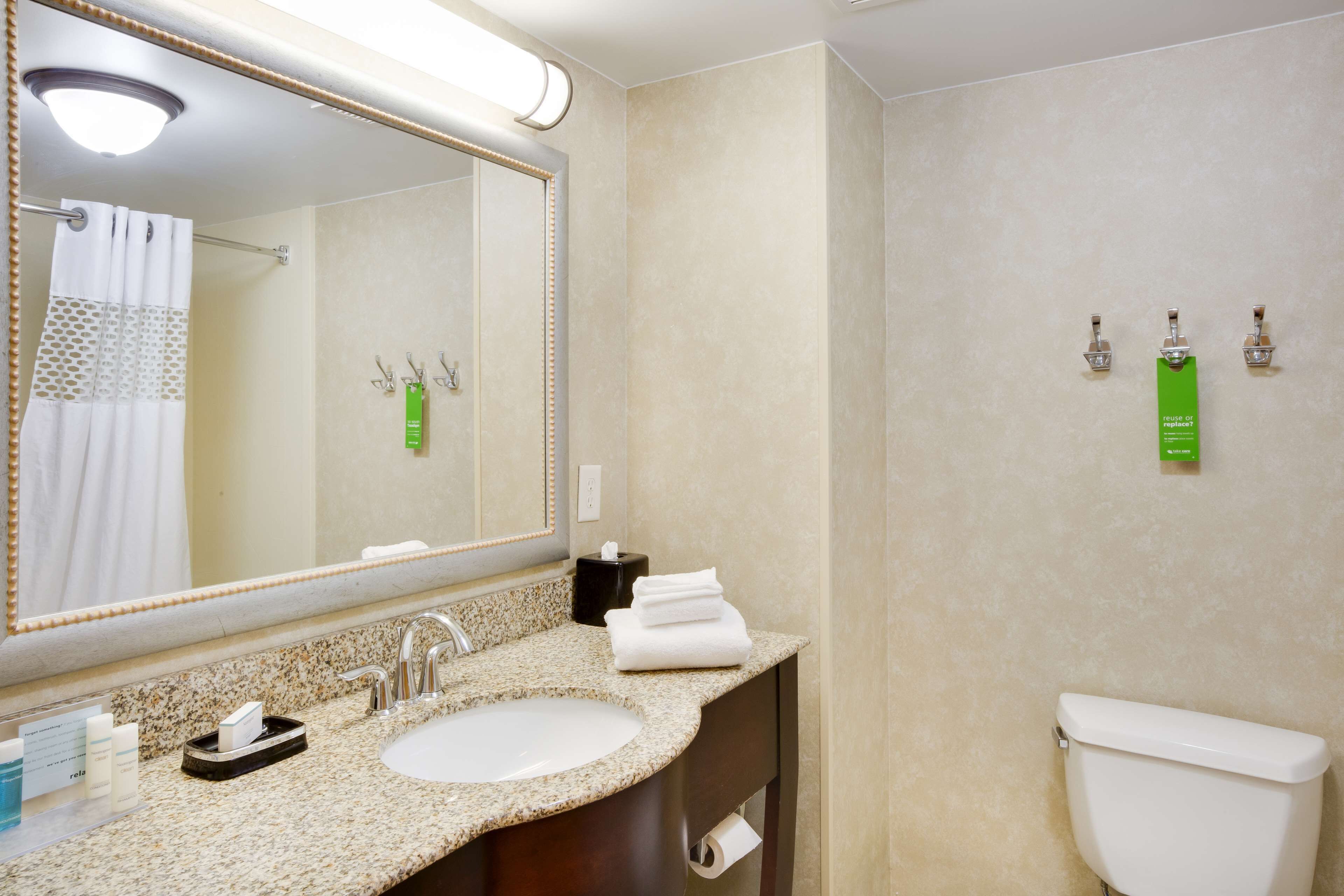 A bathroom with a sink, mirror, and toilet. There are toiletries on the counter and a towel rack.