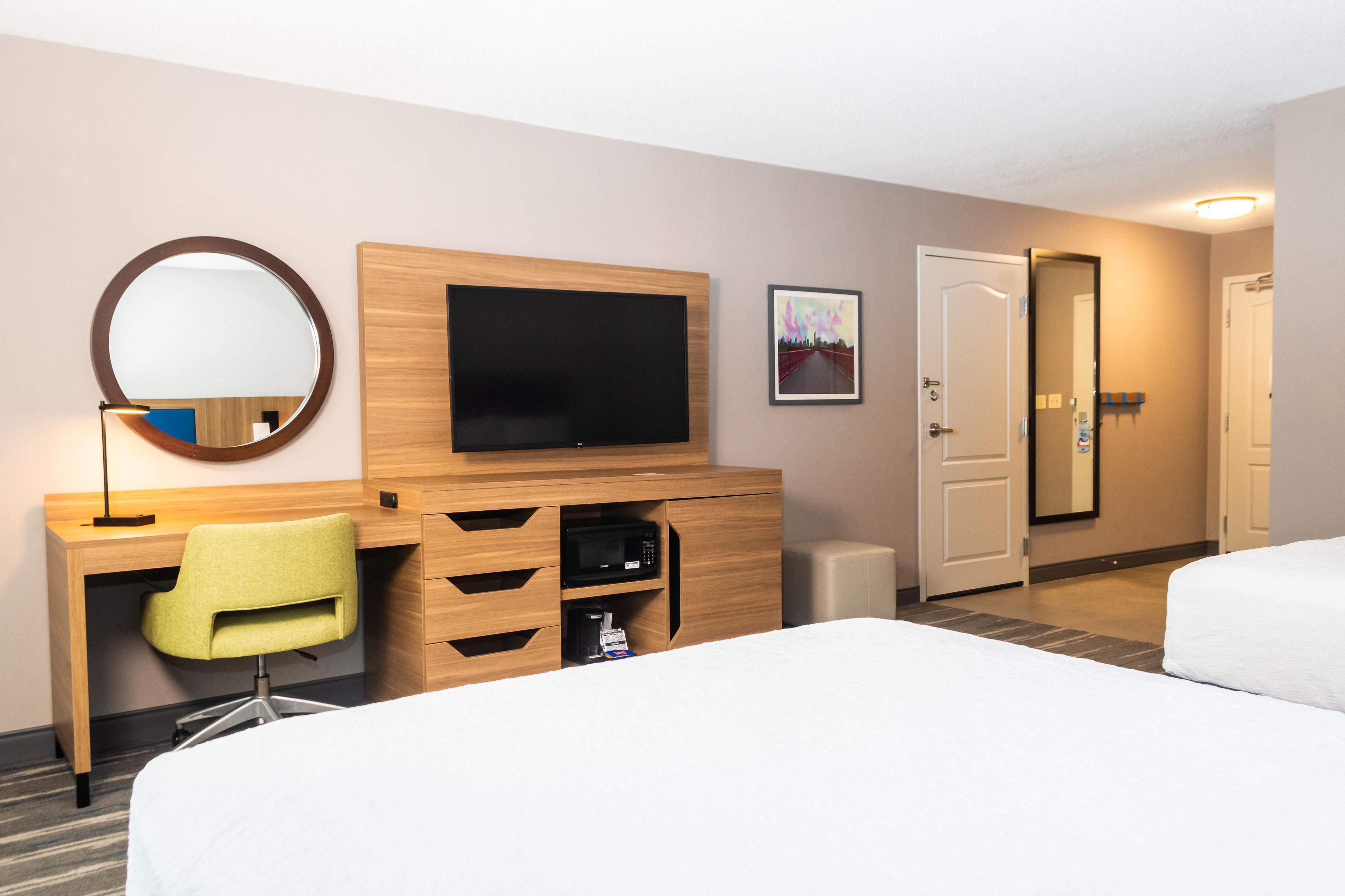 Une chambre d’hôtel comprenant un lit, un bureau avec une chaise, une télévision, un miroir et une porte.