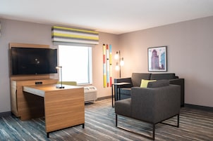 Habitación de hotel con escritorio, televisión de pantalla plana, sofá, ventana con vistas y aire acondicionado instalado en la pared.