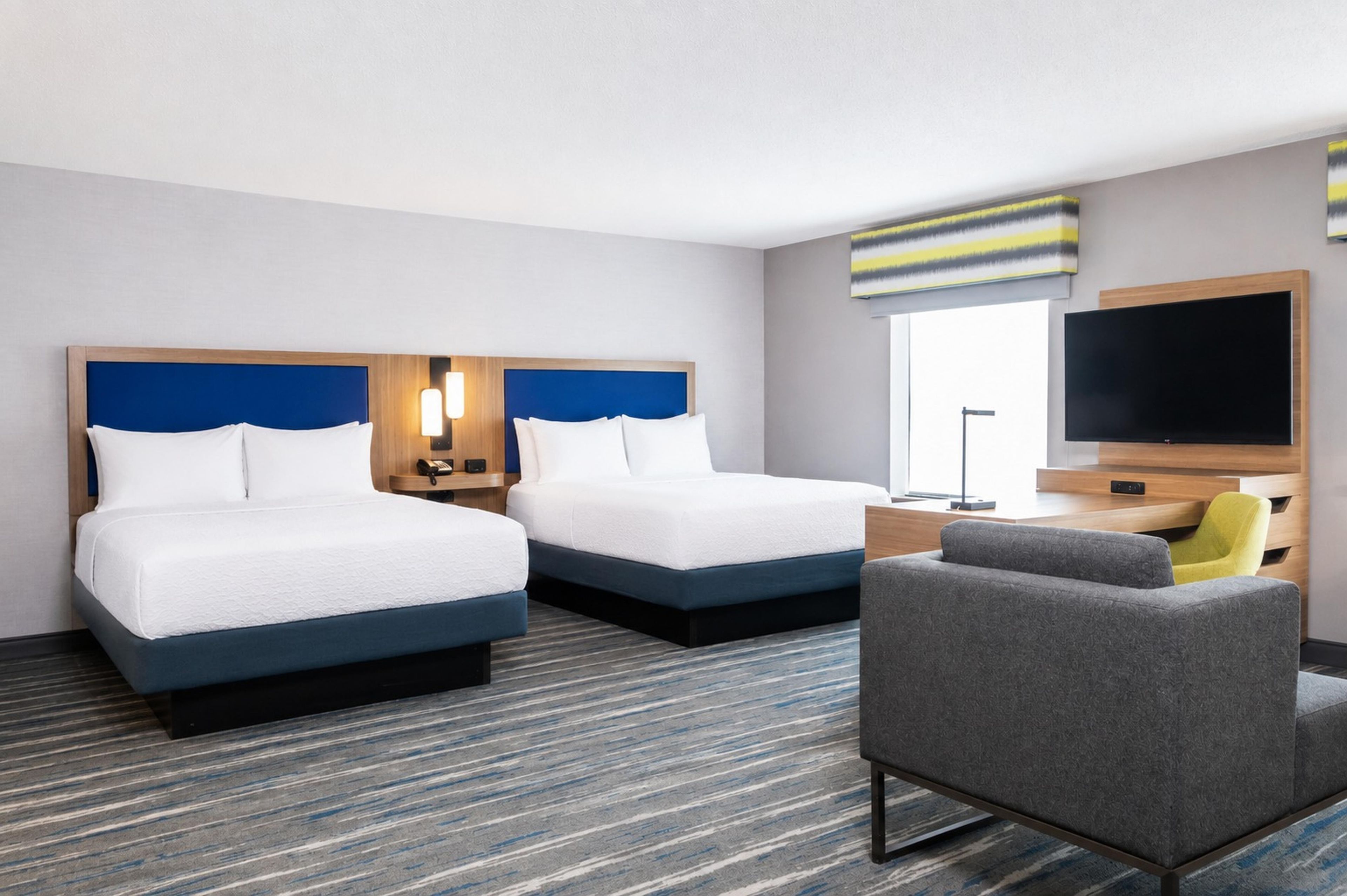 Ein Hotelzimmer mit zwei Betten, einem Schreibtisch, einem Stuhl, einem Fernseher und einem Fenster.