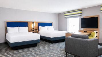 Ein Hotelzimmer mit zwei Betten, einem Schreibtisch, einem Stuhl, einem Fernseher und einem Fenster.