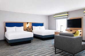 Een hotelkamer met twee bedden, een bureau, een stoel, een televisie en een raam.