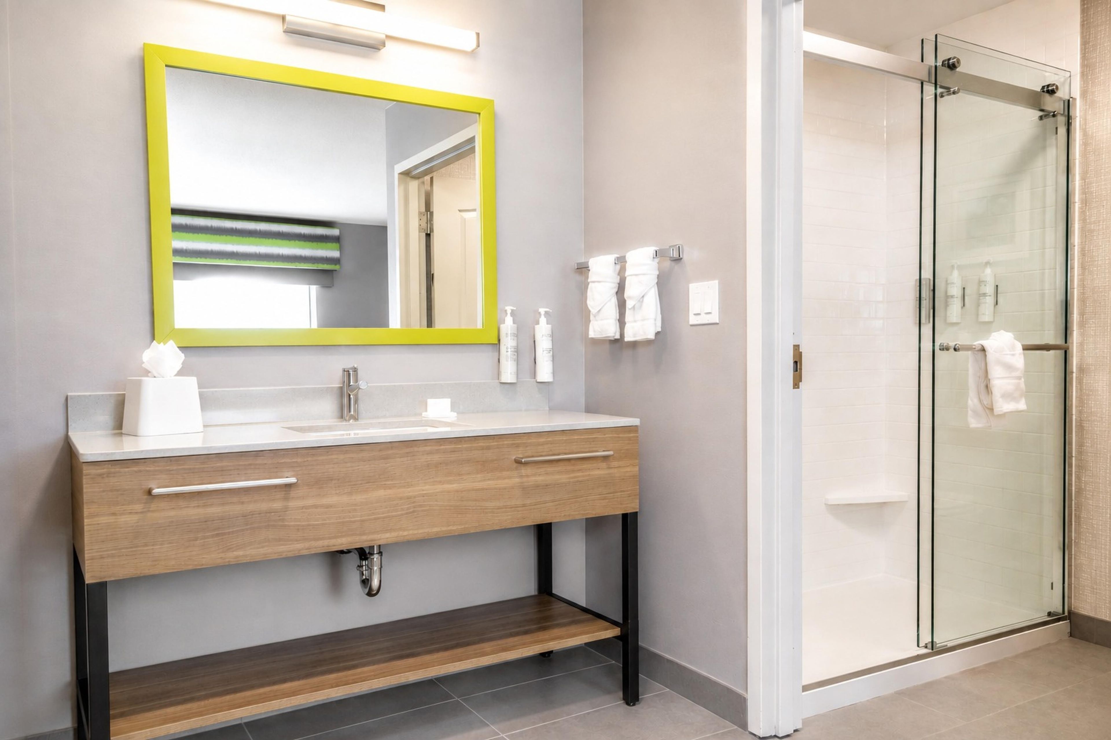 A modern bathroom with a wooden vanity, a mirror with a yellow frame, and a glass shower enclosure.