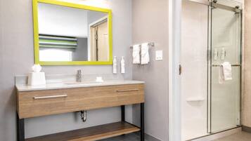 A modern bathroom with a wooden vanity, a mirror with a yellow frame, and a glass shower enclosure.