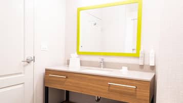 Un baño con un lavamanos blanco, tocador de madera, un espejo con marco amarillo y artículos de aseo en la pared.