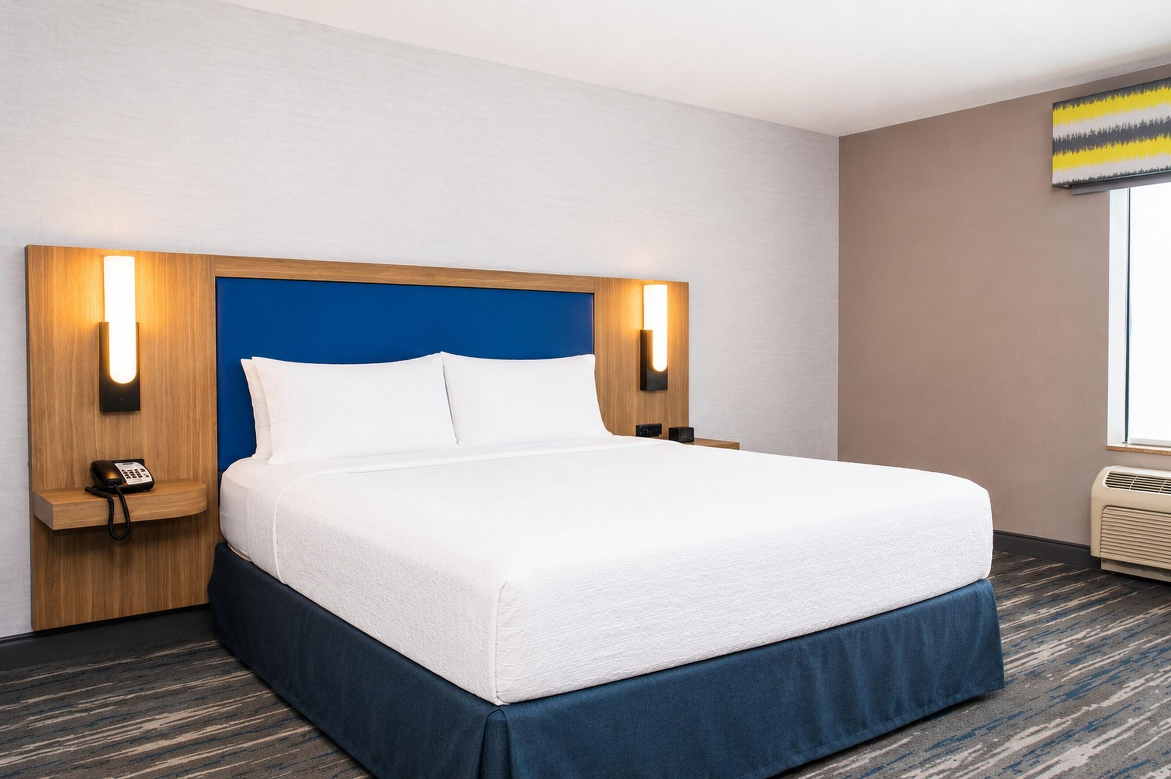 Una habitación de hotel con una cama grande, un teléfono en la mesita de noche y una lámpara de pared.