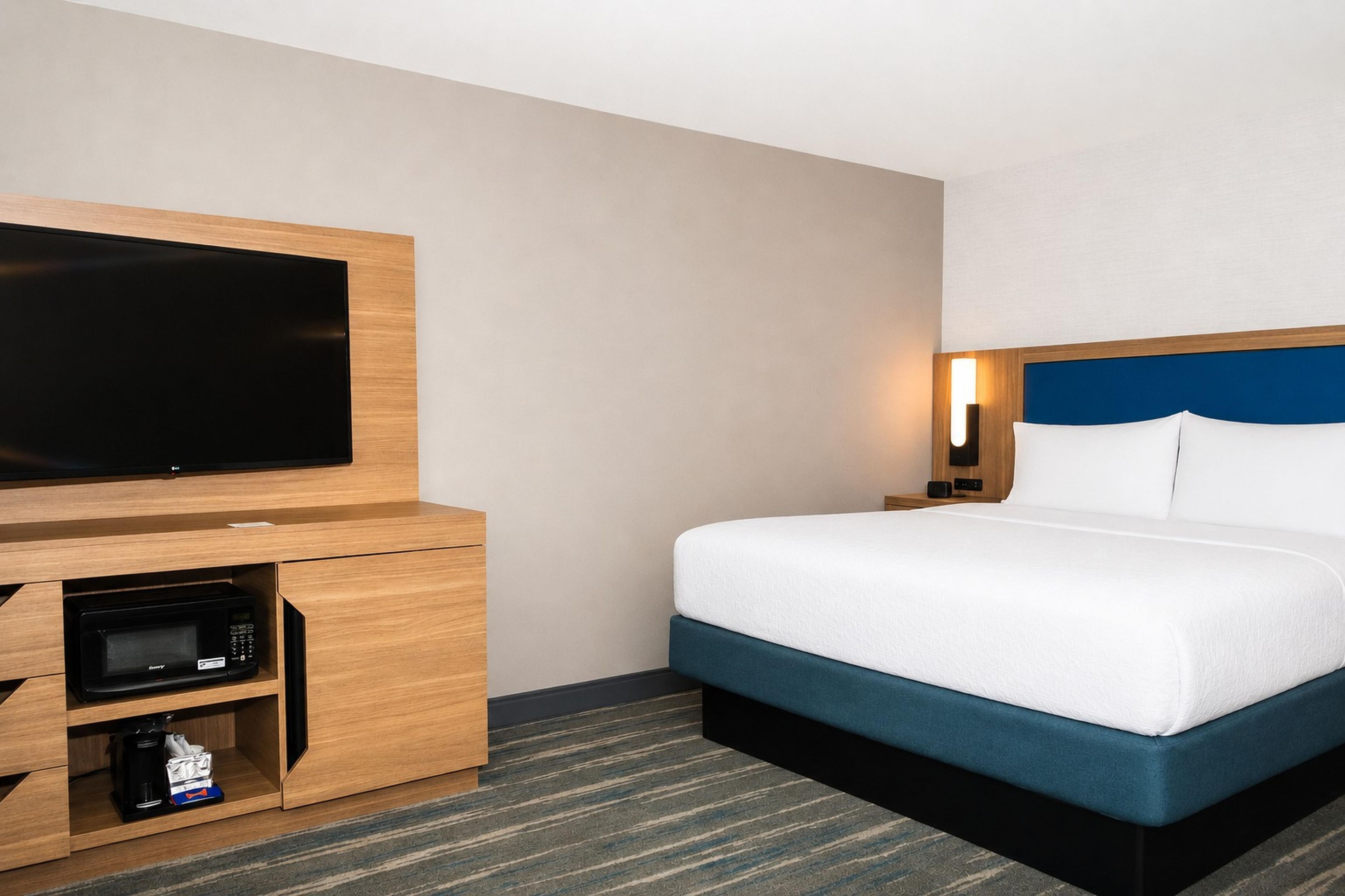 Una habitación de hotel con una cama, televisor, cafetera y mesita de noche.