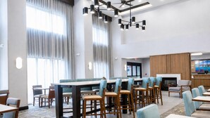 A modern dining area with high tables and bar stools, large windows with curtains, and a ceiling fan.