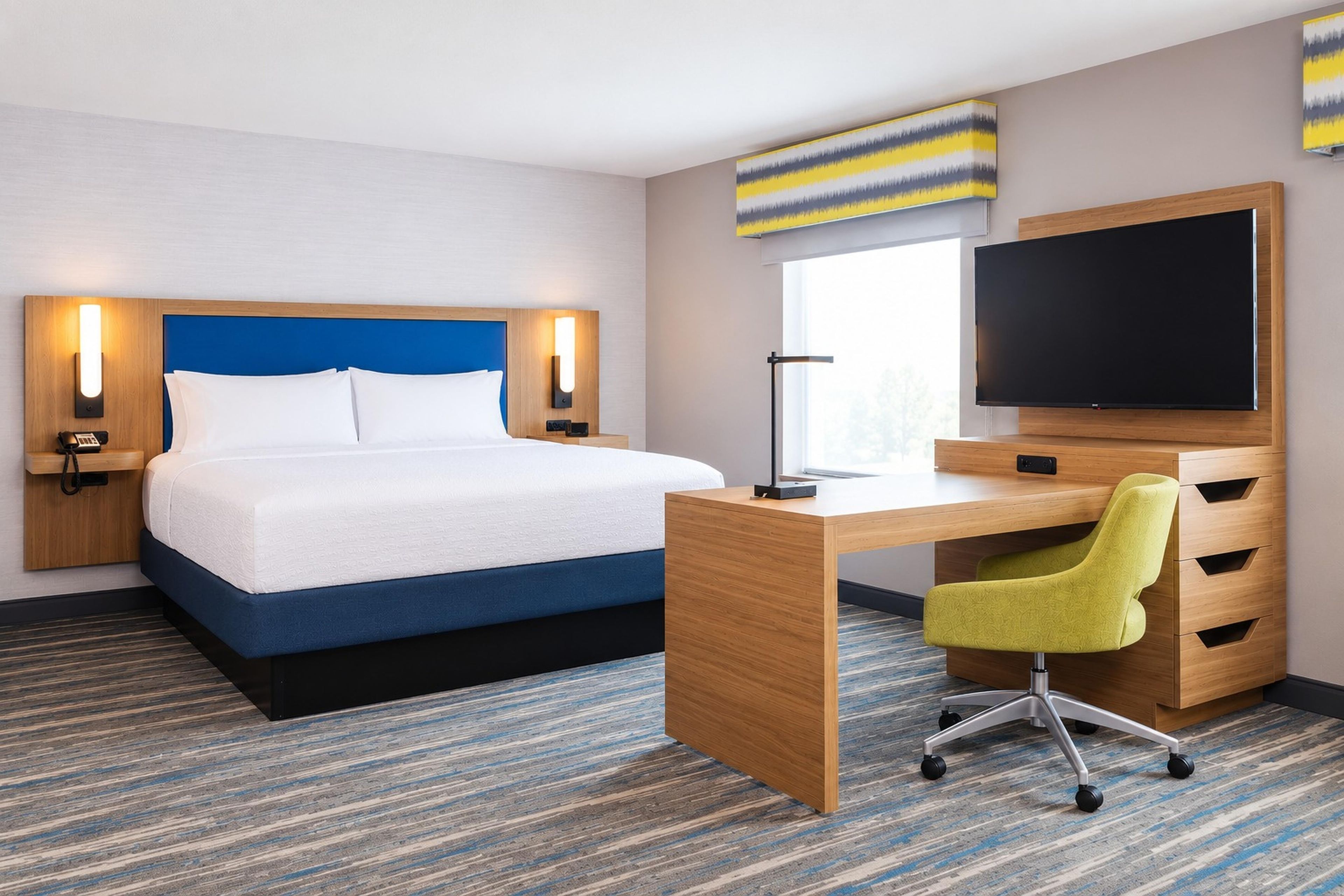 A hotel room with a bed, desk, chair, and a flat-screen TV.