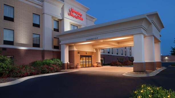 Entree van een Hampton Inn & Suites hotel met een duidelijk bord, een overdekte doorgang en een aangelegde tuin met planten.