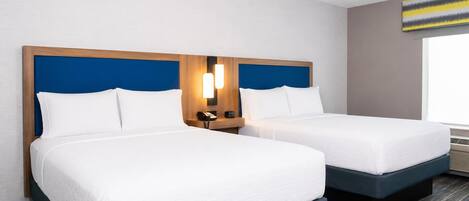 Habitació d'hotel amb dos llits, un panell de capçalera de fusta, una taula de nit amb una làmpada i una finestra amb vistes.