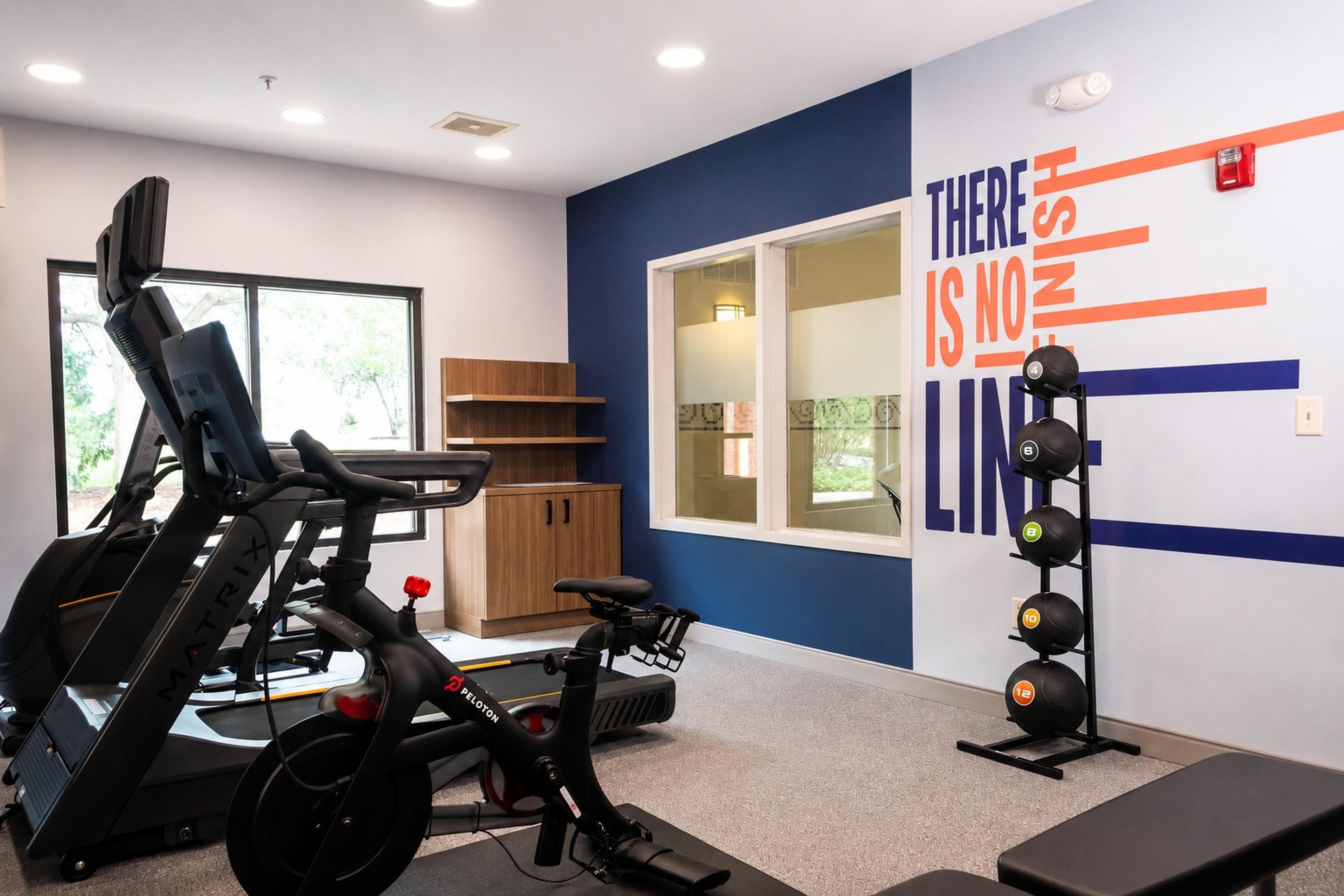 Un gimnasio con equipo de ejercicio, una pared con texto motivacional y un ventanal que deja entrar luz natural.