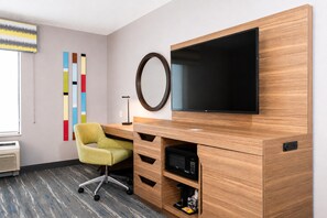 Ett modernt hotellrum med ett skrivbord i trä, en platt-TV, en stol och en spegel som är monterad på väggen.