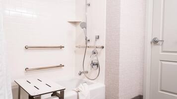 A bathroom with a white tiled wall, a shower with a handheld showerhead, a grab bar, a towel rack, and a toilet.