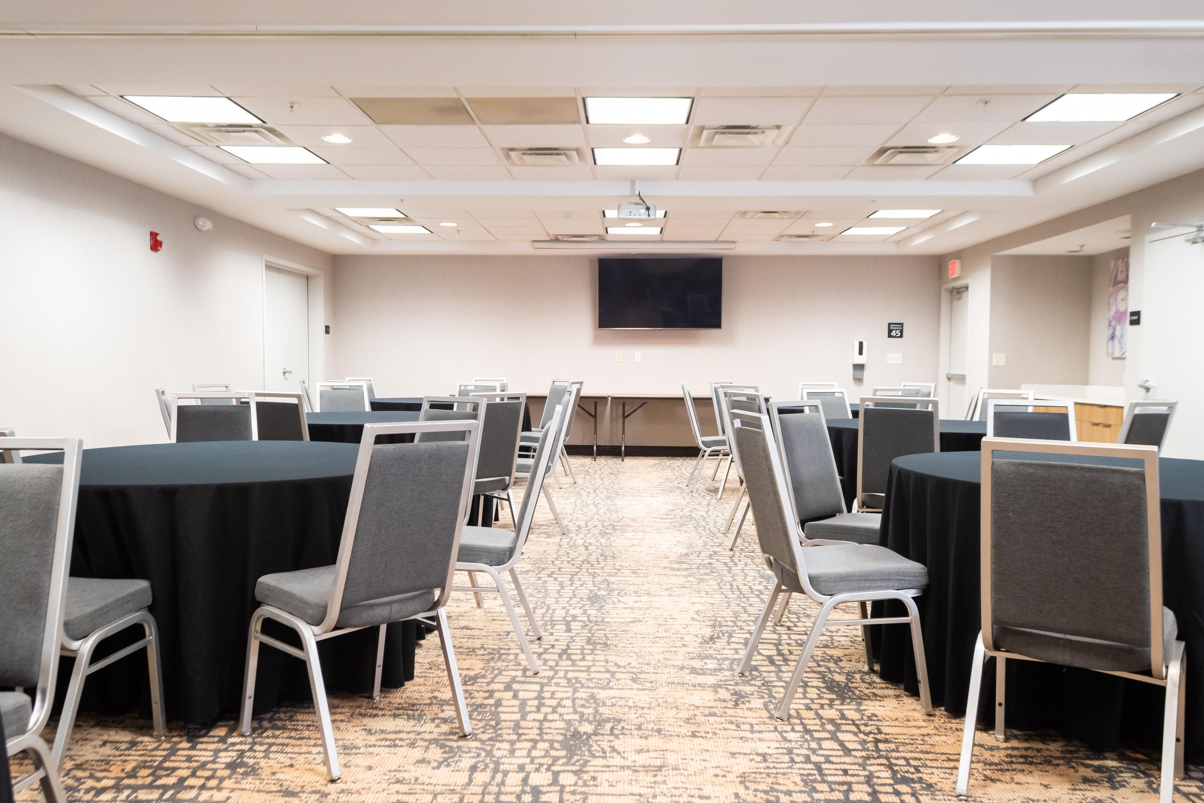 Una sala conferenze con file di tavoli e sedie, uno schermo per proiettore e un pavimento rivestito di moquette.