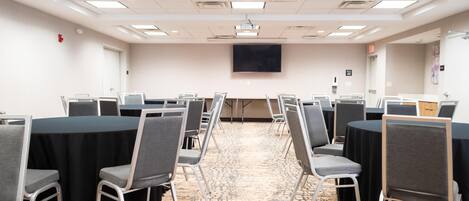 A conference room with rows of tables and chairs, a projector screen, and a carpeted floor.