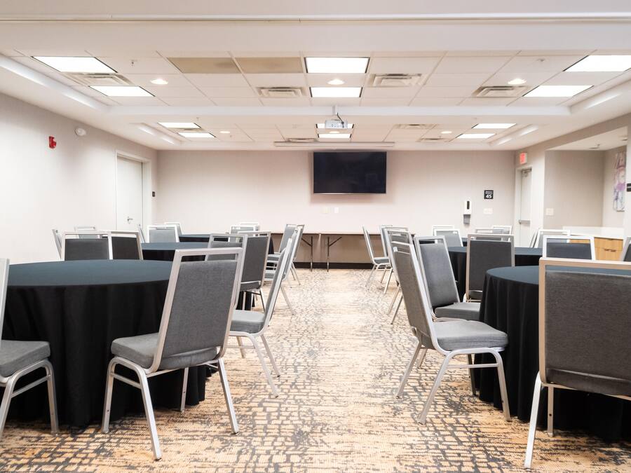 A conference room with rows of tables and chairs, a projector screen, and a carpeted floor.