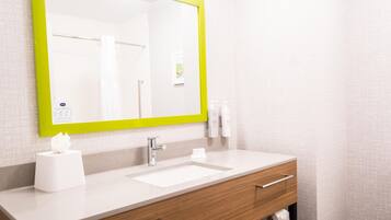 A bathroom with a white sink, a mirror with a green frame, a towel dispenser, and a toilet paper holder.