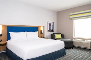 Habitación de hotel con una cama grande, una silla, un cuadro en la pared y una ventana con vistas.