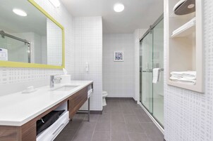 Un baño moderno con tocador blanco, un espejo grande, cabina de ducha de vidrio y azulejos estampados.