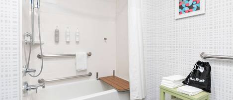 Een moderne badkamer met een badkuip, douche, handgrepen, een houten plank en een handdoekrek met handdoeken.