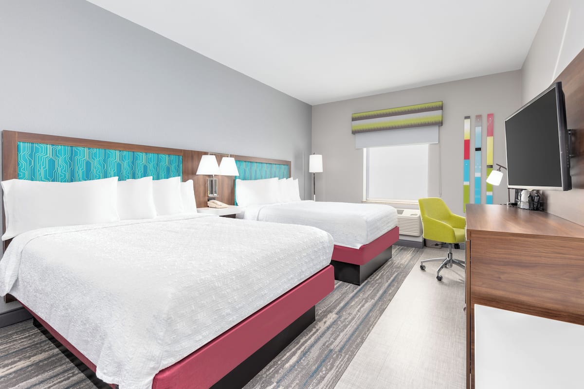 A hotel room with two beds, a desk, a TV, and a chair.