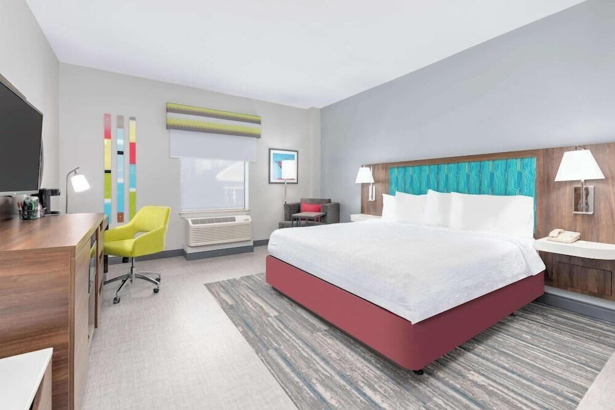 A modern hotel room with a large bed, a desk, a chair, and a window.