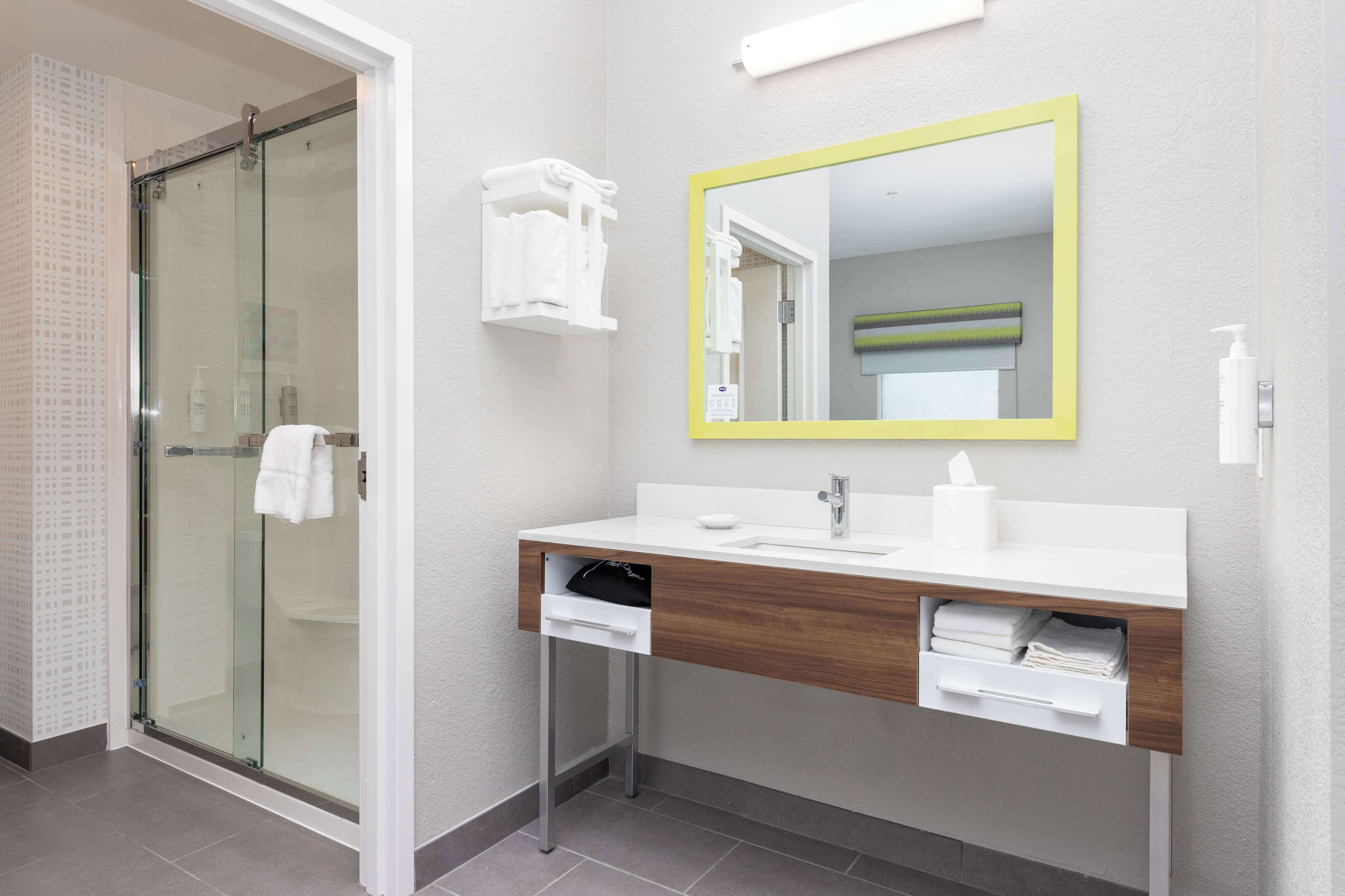 A modern bathroom with a glass shower enclosure, a white vanity with a wooden countertop, and a mirror with a yellow frame.