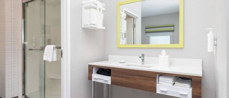 A modern bathroom with a glass shower enclosure, a white vanity with a wooden countertop, and a mirror with a yellow frame.
