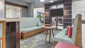 A modern hotel lobby with a seating area, a television, and a coffee machine. - Hampton Inn & Suites Lake Jackson-Clute (Clute)