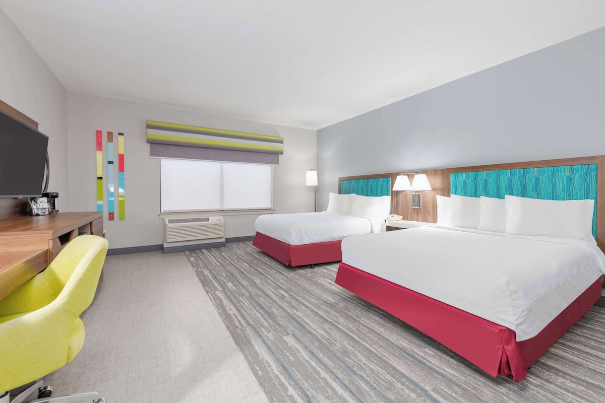 A hotel room with two beds, a desk, a chair, a TV, and a window with curtains.