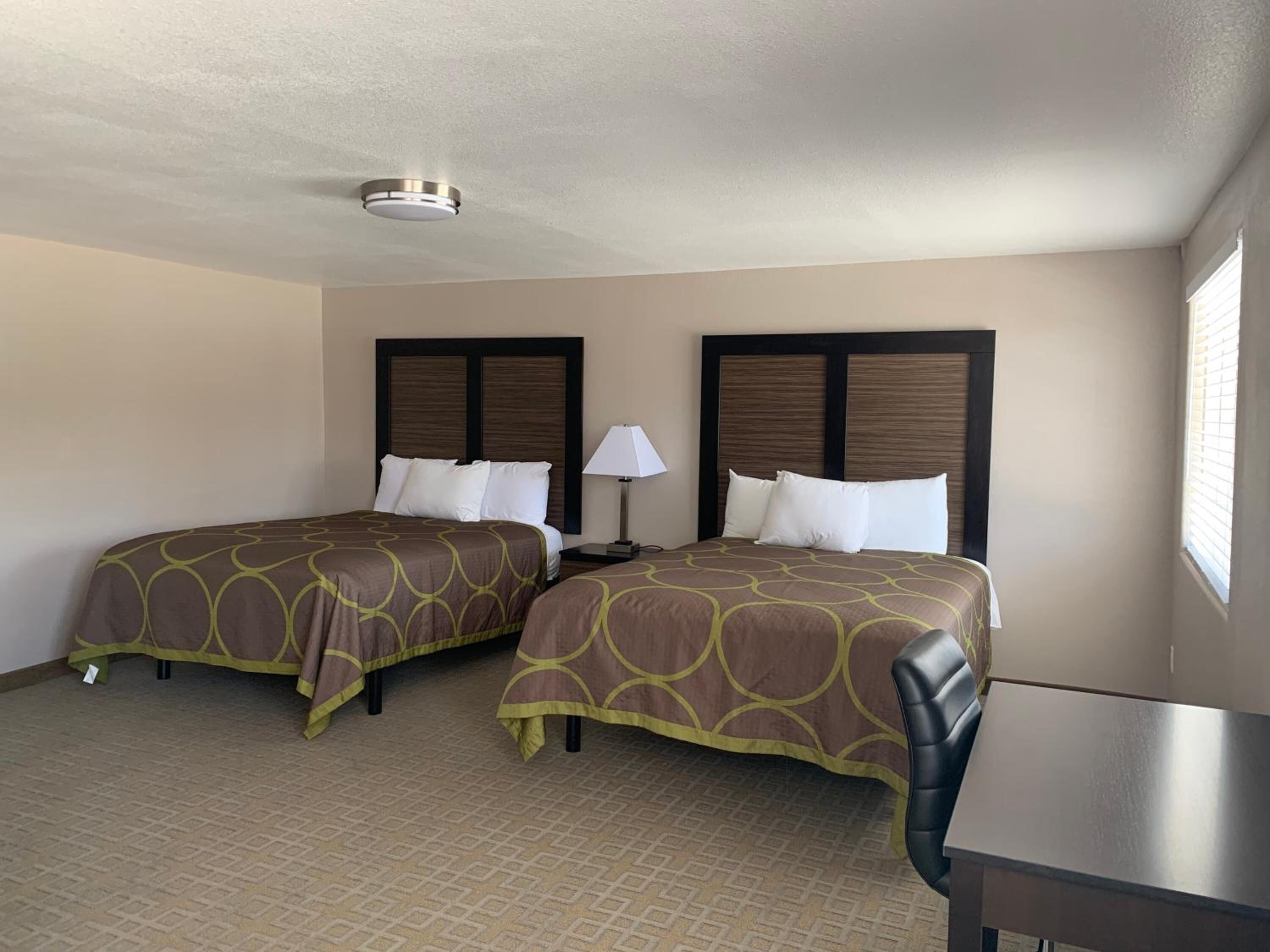 Una habitación de hotel con dos camas, una mesita de noche, una lámpara y un ventanal con persianas.