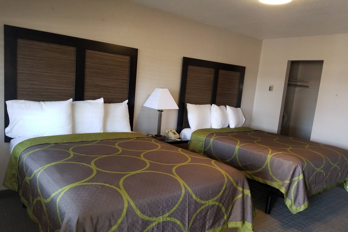 A hotel room with two beds, each with a patterned bedspread, a bedside lamp, and a telephone.