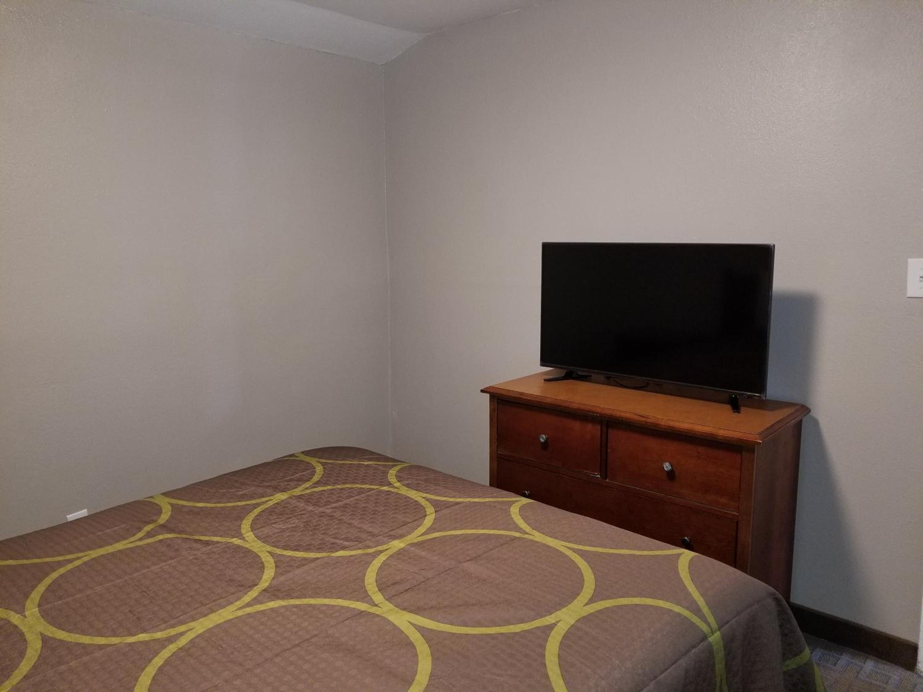 A small, single-bed room with a wooden dresser and a television on top.