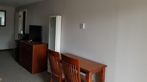 A hotel room with a wooden desk, two chairs, a television, and a wall-mounted air conditioner. - Beverly Lodge (South Lake Tahoe)