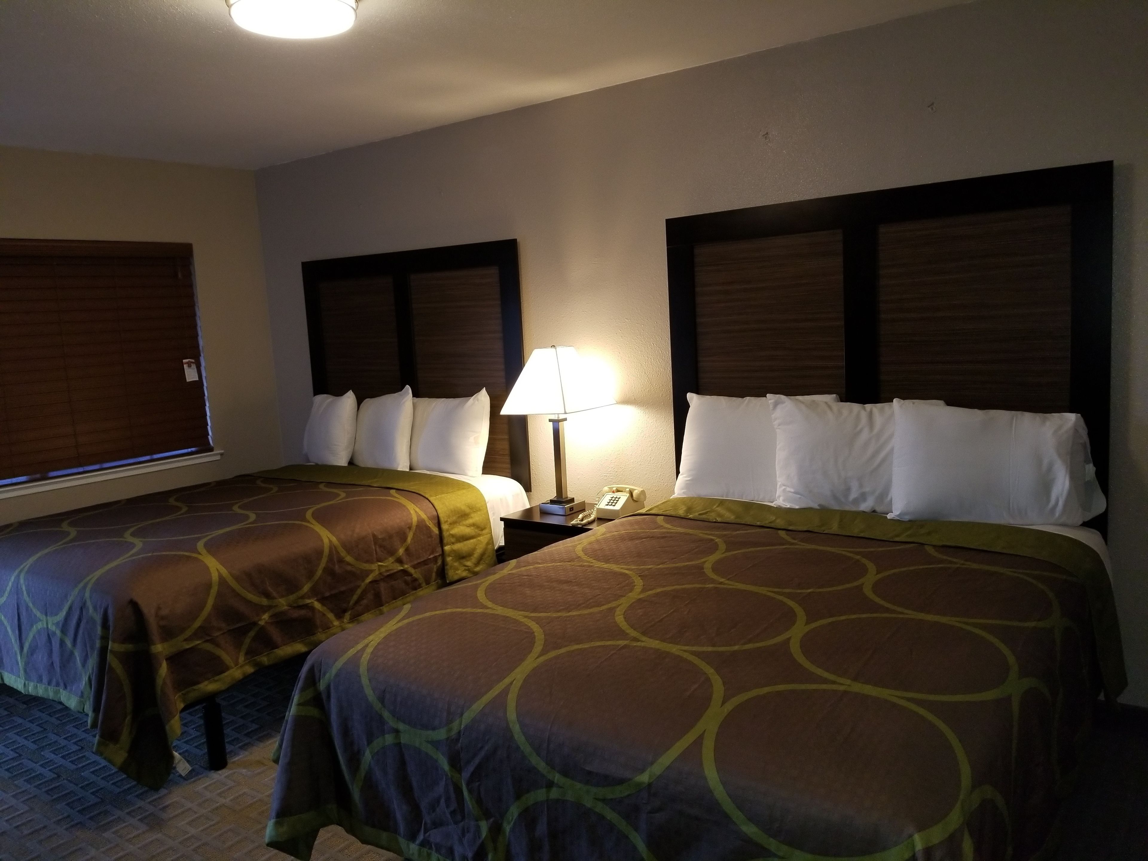 Habitación de hotel con dos camas, cada una con cabecero, mesita de noche con lámpara y teléfono.