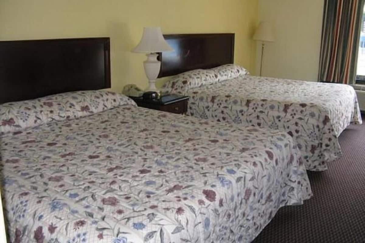 Een hotelkamer met twee bedden, elk met bloemenbedrukte lakens, een nachtkastje met een lamp, en een raam met gordijnen.