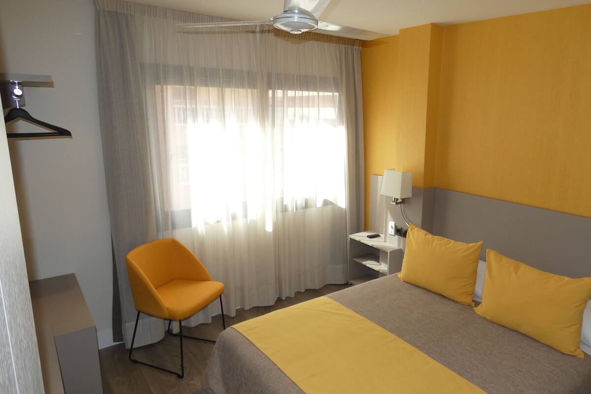 Ein Hotelzimmer mit Bett, Stuhl, Schreibtisch und einem Fenster mit Vorhängen.