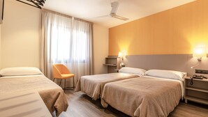 Una habitación de hotel con dos camas, una silla, un escritorio con lámpara y un ventilador de techo.