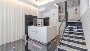 Un área de recepción de hotel moderna, con un mostrador blanco, una escalera de cristal y un suelo limpio y pulido.