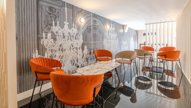 Un comedor moderno con una mesa de mármol y sillas color naranja, un mural decorativo y un suelo reflectante.