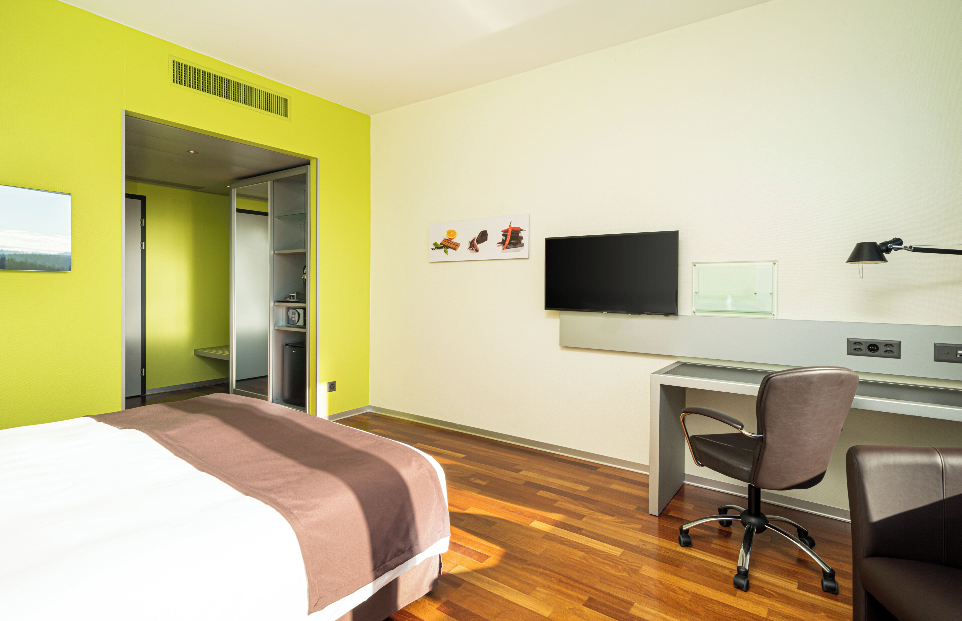 Une chambre d’hôtel avec un lit, un bureau, une chaise, une télévision et un tableau au mur.